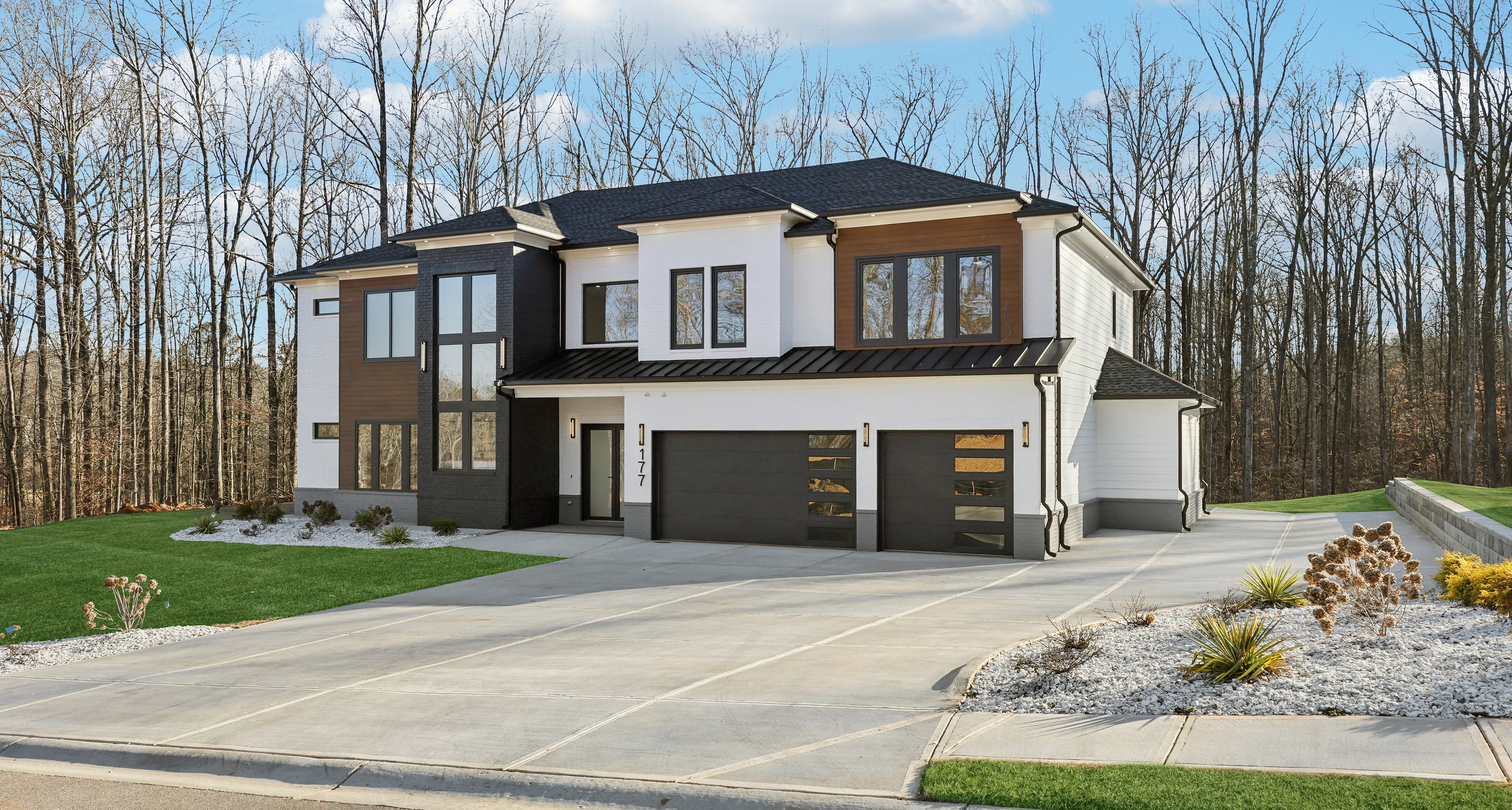 Front elevation of the 177 Deer Canyon Rd home photographed from an angle, showing the garage bays, landscaped bed, and dark wood entry surround