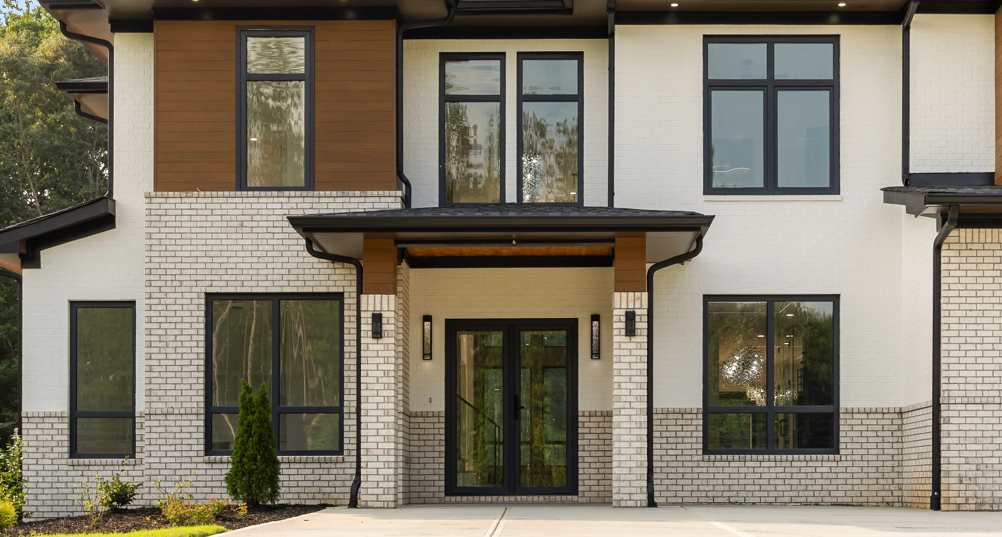 Front elevation of 816 Riverside in daylight: painted brick with wood accent panels, black window frames, and a three-car garage set into a sloped lot