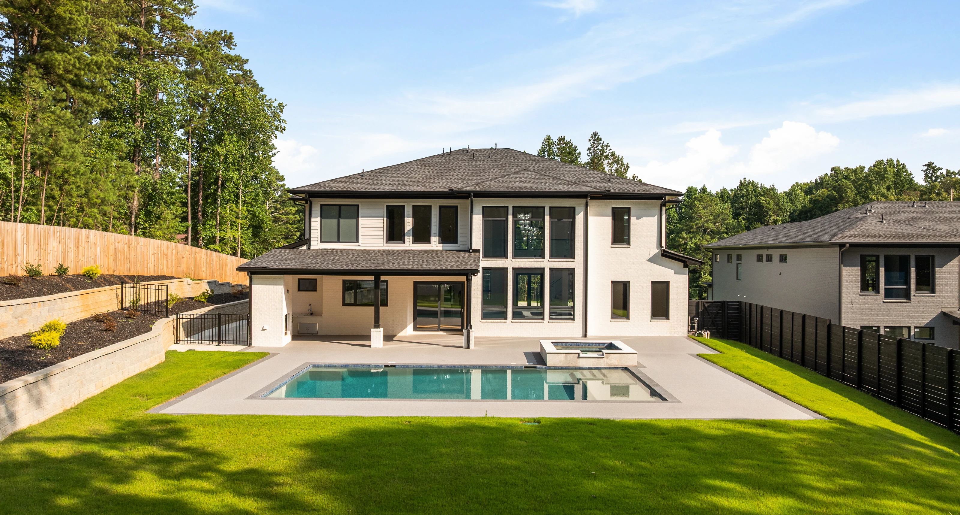 Backyard at 816 Riverside in daylight, showing the pool, concrete deck, tiered lawn, and retaining wall below the rear of the house