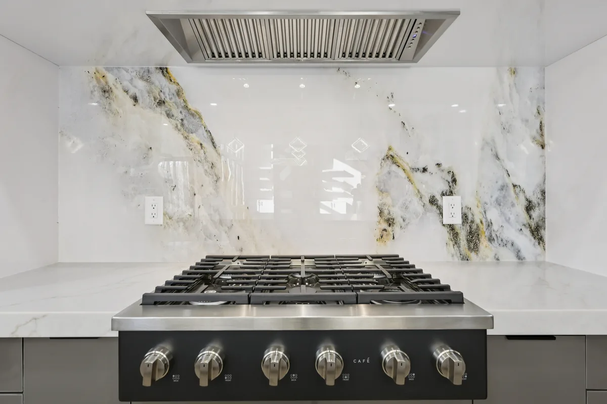 Close view of the bookmatched marble slab behind the range, with gold and grey veining and a stainless hood above