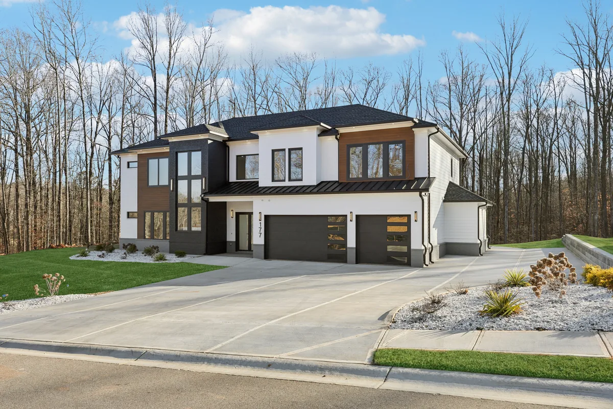 Front elevation photographed from an angle, showing the two-car and single-car garage bays, landscaped bed, and dark wood entry surround