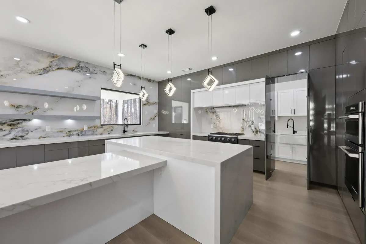 Kitchen island in veined marble with a waterfall edge, pendant lights above, and dark cabinetry along the back wall