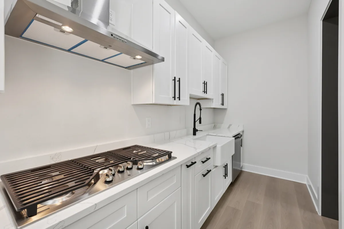 Separate prep kitchen with white shaker cabinetry, a black faucet, quartz counters, and a secondary cooktop