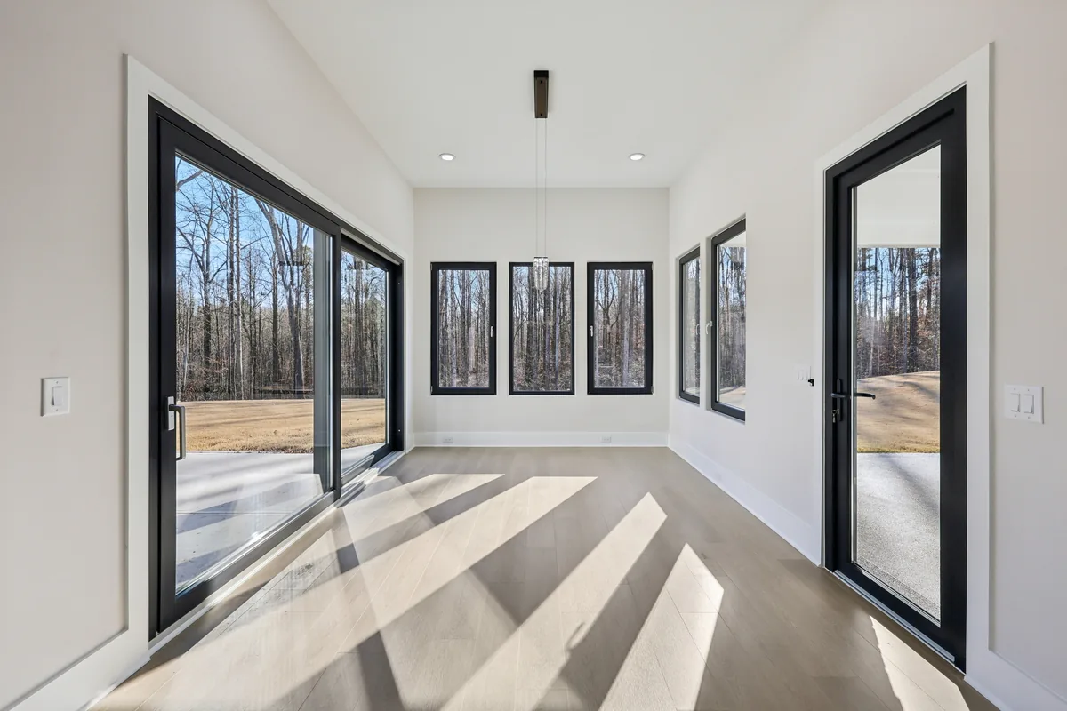 Breakfast nook with a pendant light, black-framed windows on three sides, and a sliding door opening to the rear yard