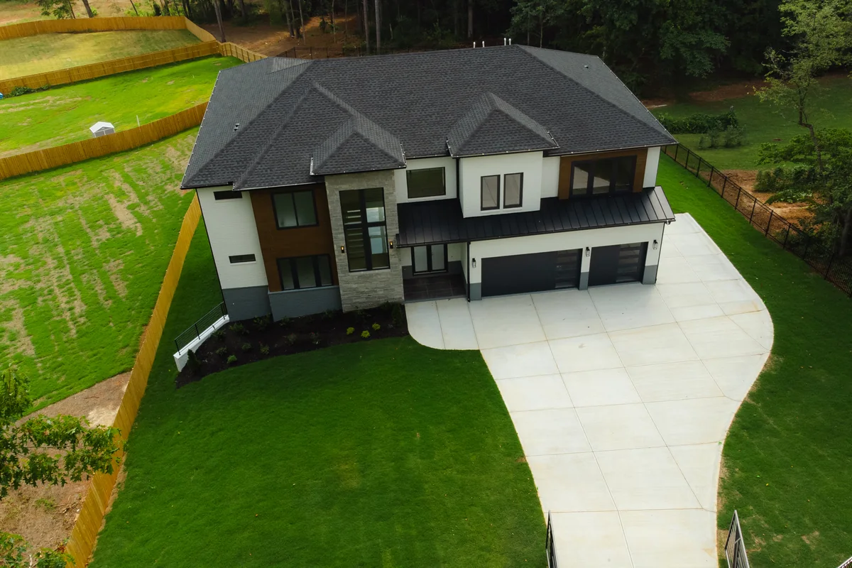 Aerial view of the home and its curved driveway, showing the hipped roof, the lawn, and the surrounding tree line