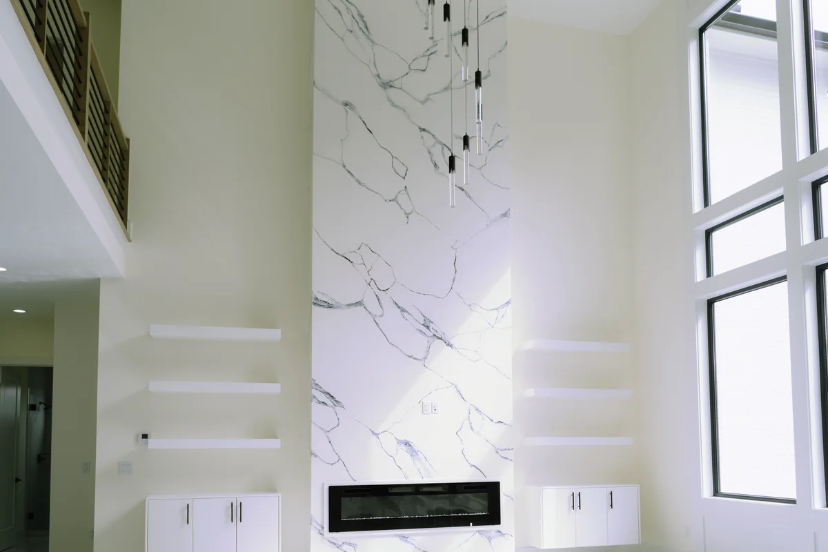Two-story living room with a full-height marble-look slab fireplace wall, a linear gas fire, flanking white cabinetry, and a rail-edged walkway above