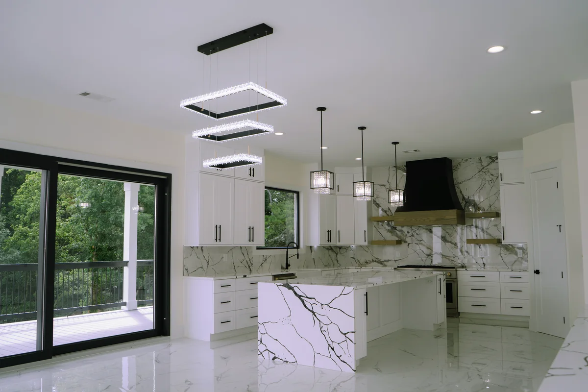 Open kitchen with a waterfall marble-look island, white cabinetry, a black hood, layered rectangular ceiling lights, and sliding glass out to the porch