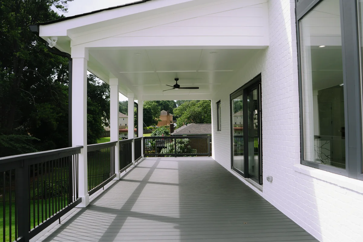 Long covered rear porch with a white tongue-and-groove ceiling, ceiling fans, black railings, and sliding glass doors along the house wall