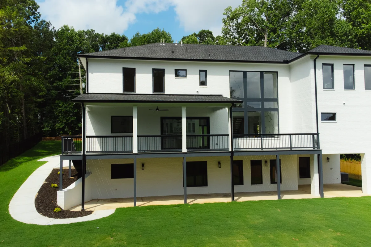Rear elevation with a covered upper deck, a walkout lower level, black metal railings, and lawn sloping down to the tree line
