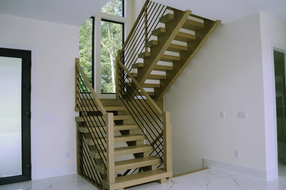 Open stair with pale oak treads, open risers, and a black horizontal metal rail set against plain white walls