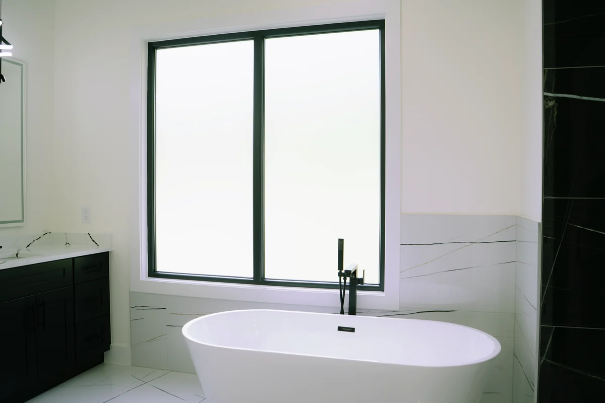 Primary bathroom with a freestanding soaking tub beneath a tall black-framed window and a matte black floor-mounted filler