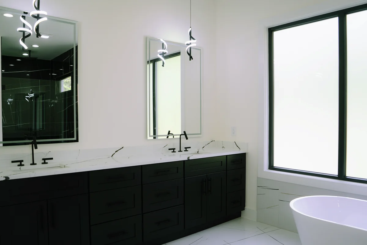 Double vanity in dark cabinetry with a white quartz counter, twin mirrors, matte black fittings, and the soaking tub beyond