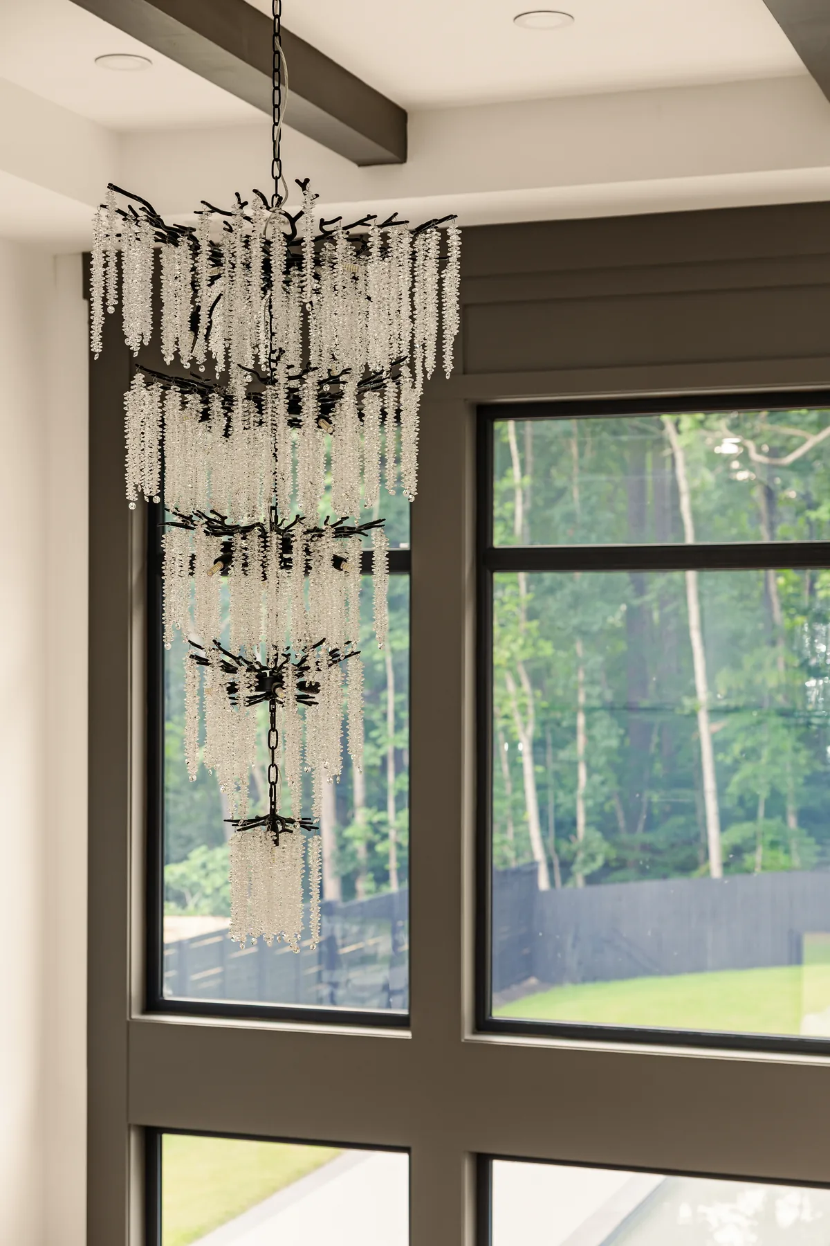 Great room chandelier: a tiered crystal chandelier above the seating area, with black-framed windows looking into the tree line
