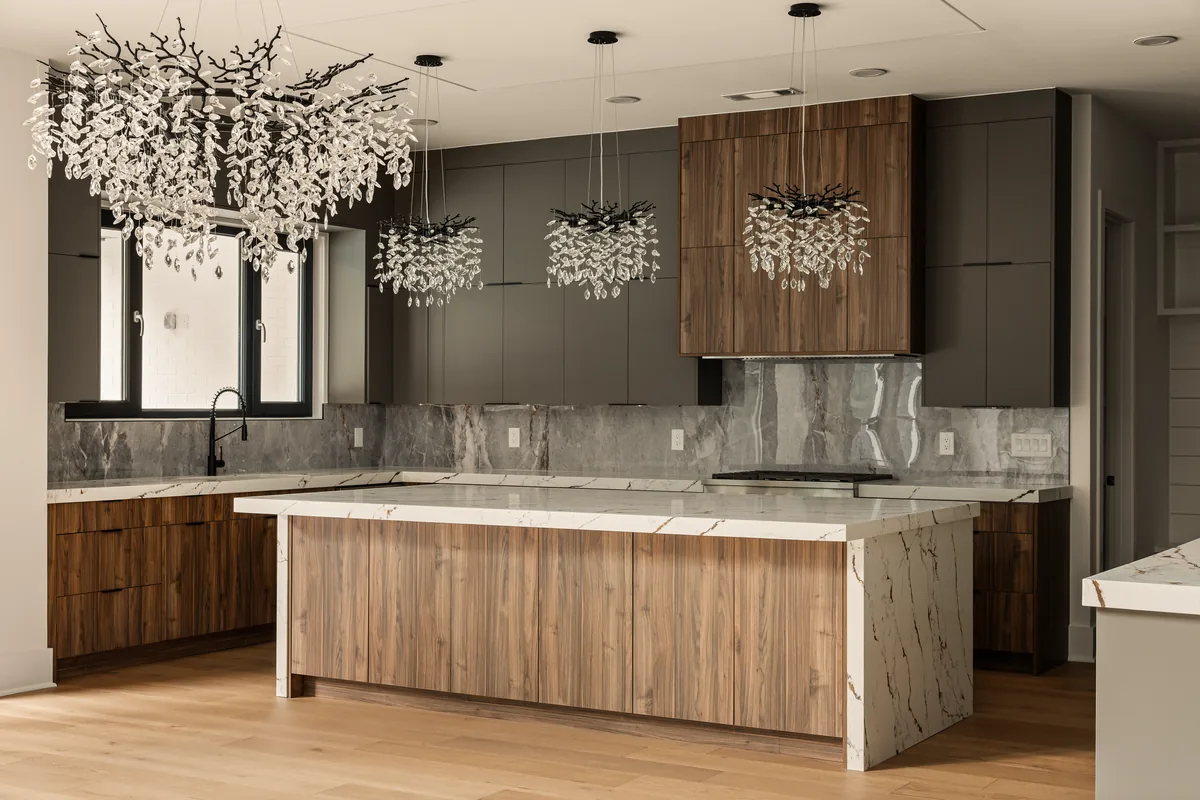 Kitchen with a large island wrapped in vertical wood slats, quartz countertops, a marble-look slab backsplash, and a pair of linear crystal pendants