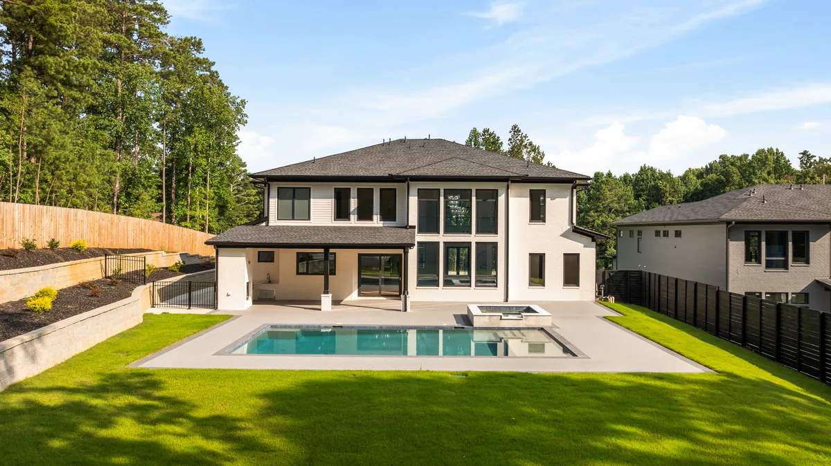 Backyard in daylight showing the pool, concrete deck, tiered lawn, and retaining wall below the rear of the house
