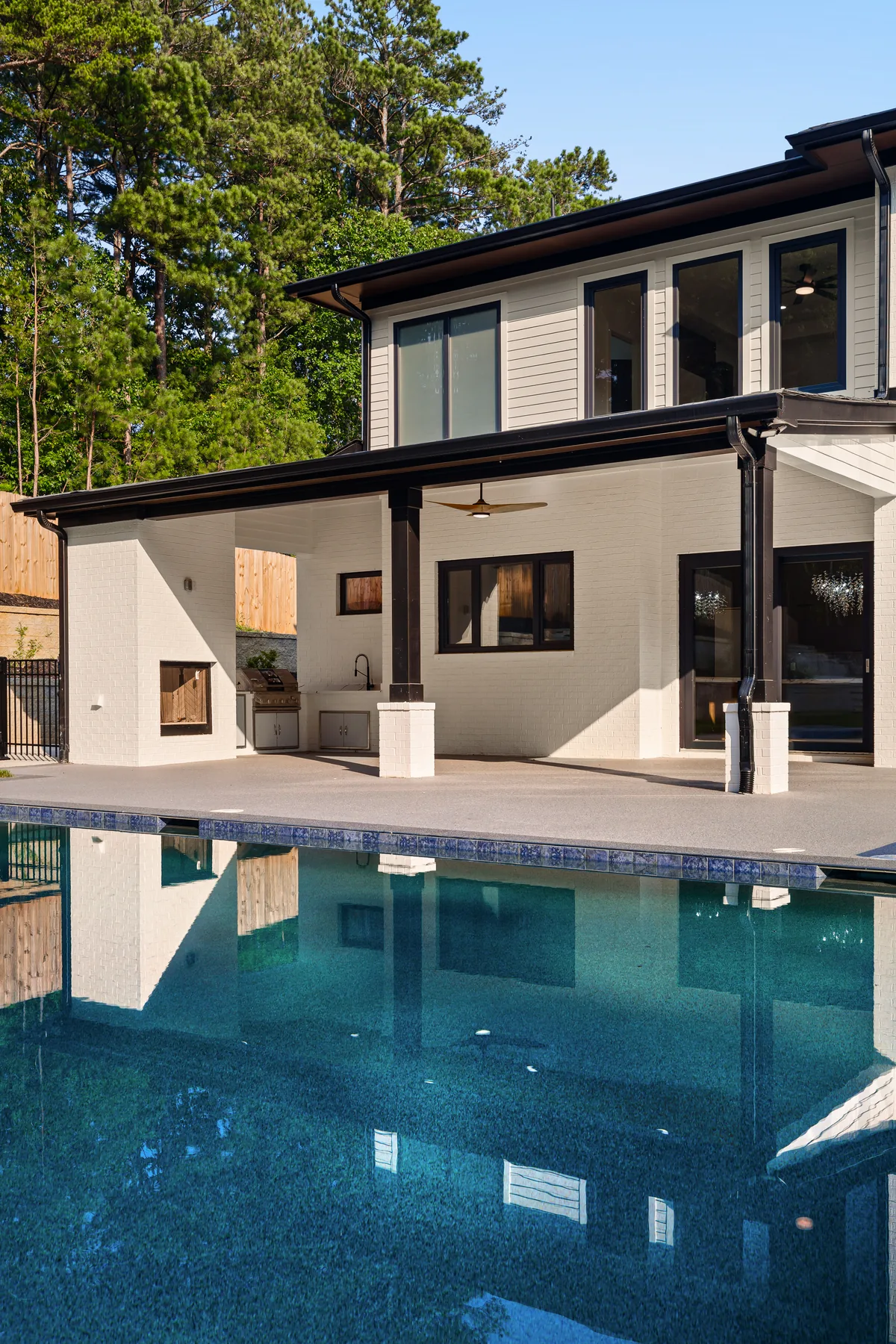 The pool in daylight with the painted brick rear elevation and covered patio behind it, reflected in the water