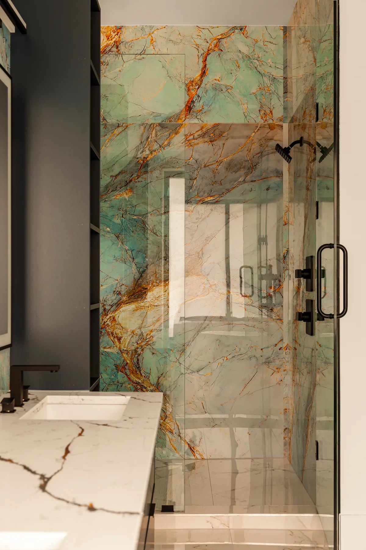 Primary shower finished in large-format veined stone slab with a matte black shower fitting and frameless glass
