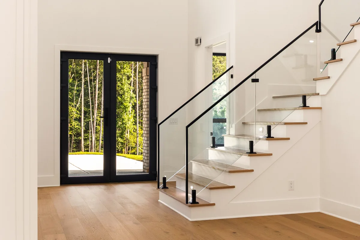 Open stair with white treads, a glass and black metal rail, and floor-to-ceiling glazing on the landing wall
