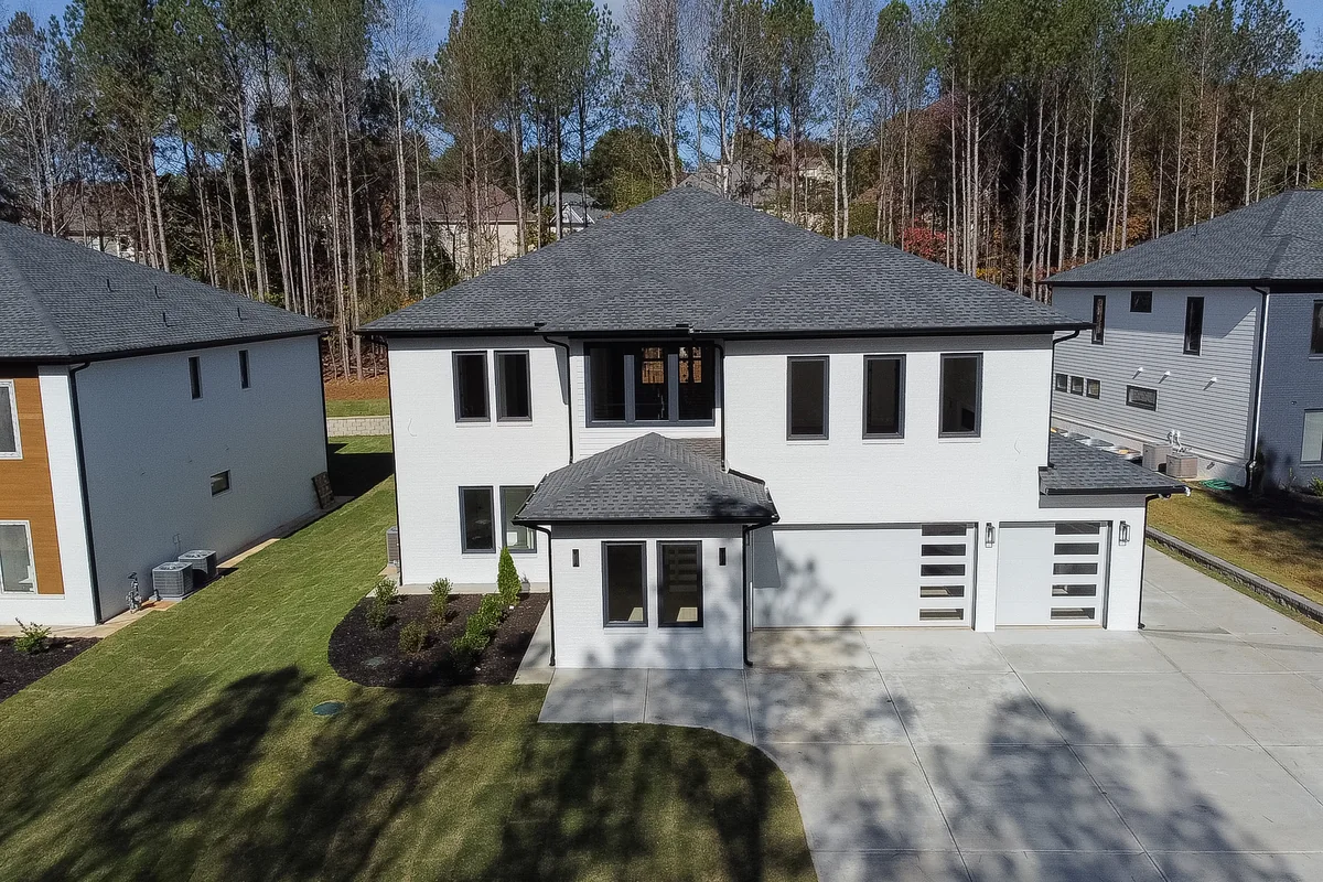 Elevated view of the finished home in its street setting, with the concrete driveway, the graded lot, and neighbouring houses along the road