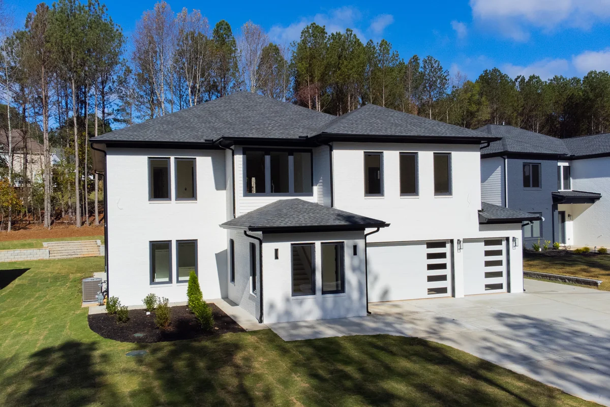 Front elevation of the 754 Riverside Rd home: a two-story white stucco facade with black-framed windows, a dark hipped roof, a covered entry, and a two-car garage on a graded lot