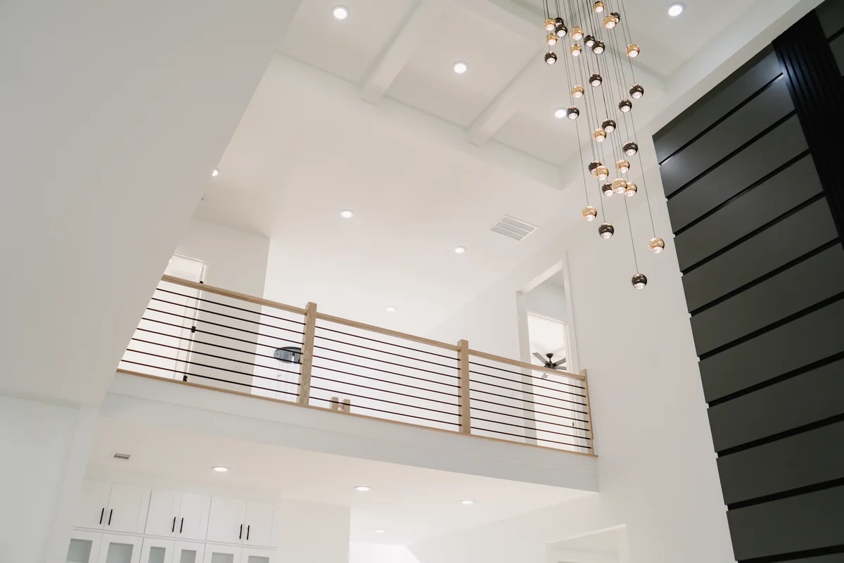Two-story great room with a black slat feature wall running the full height, a horizontal metal rail on the landing above, and a linear cluster of glass pendants