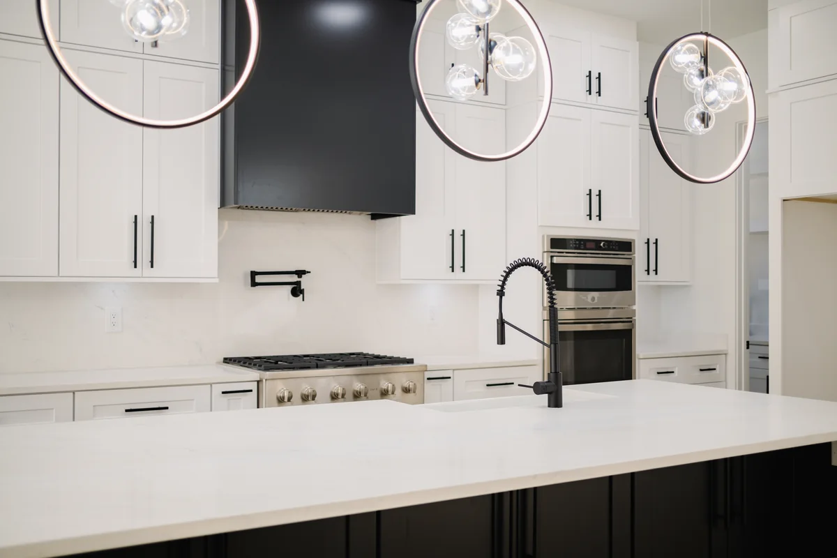 Kitchen with white cabinetry, a quartz waterfall island, a black hood over the gas range, stacked wall ovens, and matte black fittings