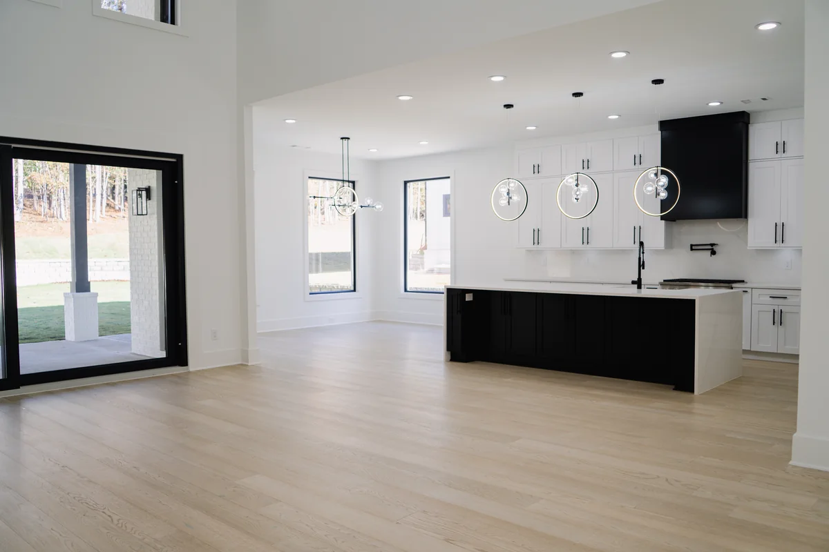 Open-plan living area with pale oak floors looking through to the kitchen, with black-framed windows on two walls