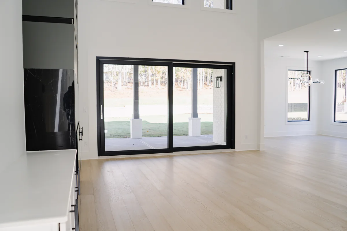 Living room with a wide black-framed sliding glass door onto the rear yard, flanked by tall windows