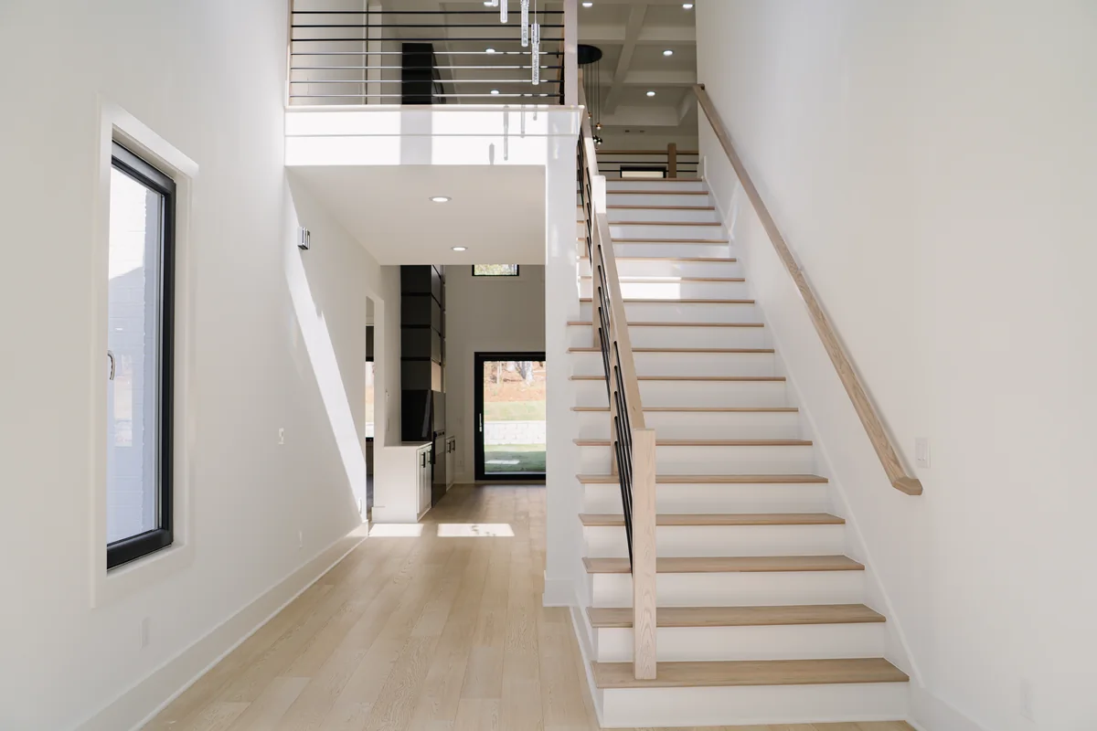 Entry stair with white risers, pale oak treads, and a black horizontal metal rail, lit by tall windows on the landing