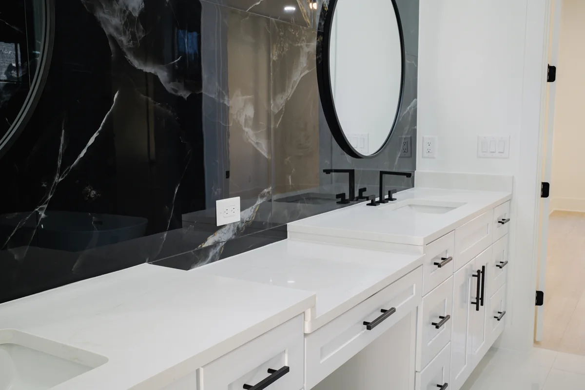 Primary bathroom vanity set against a dramatic black and white veined stone slab wall, with a round mirror, white quartz counter, and matte black fittings