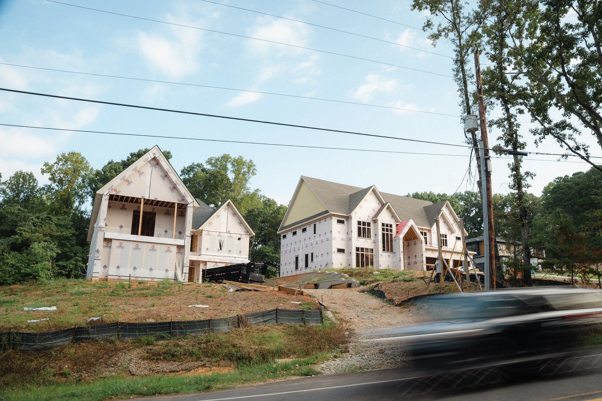 Street view of several roofed and weather-wrapped houses under construction on a sloped site.