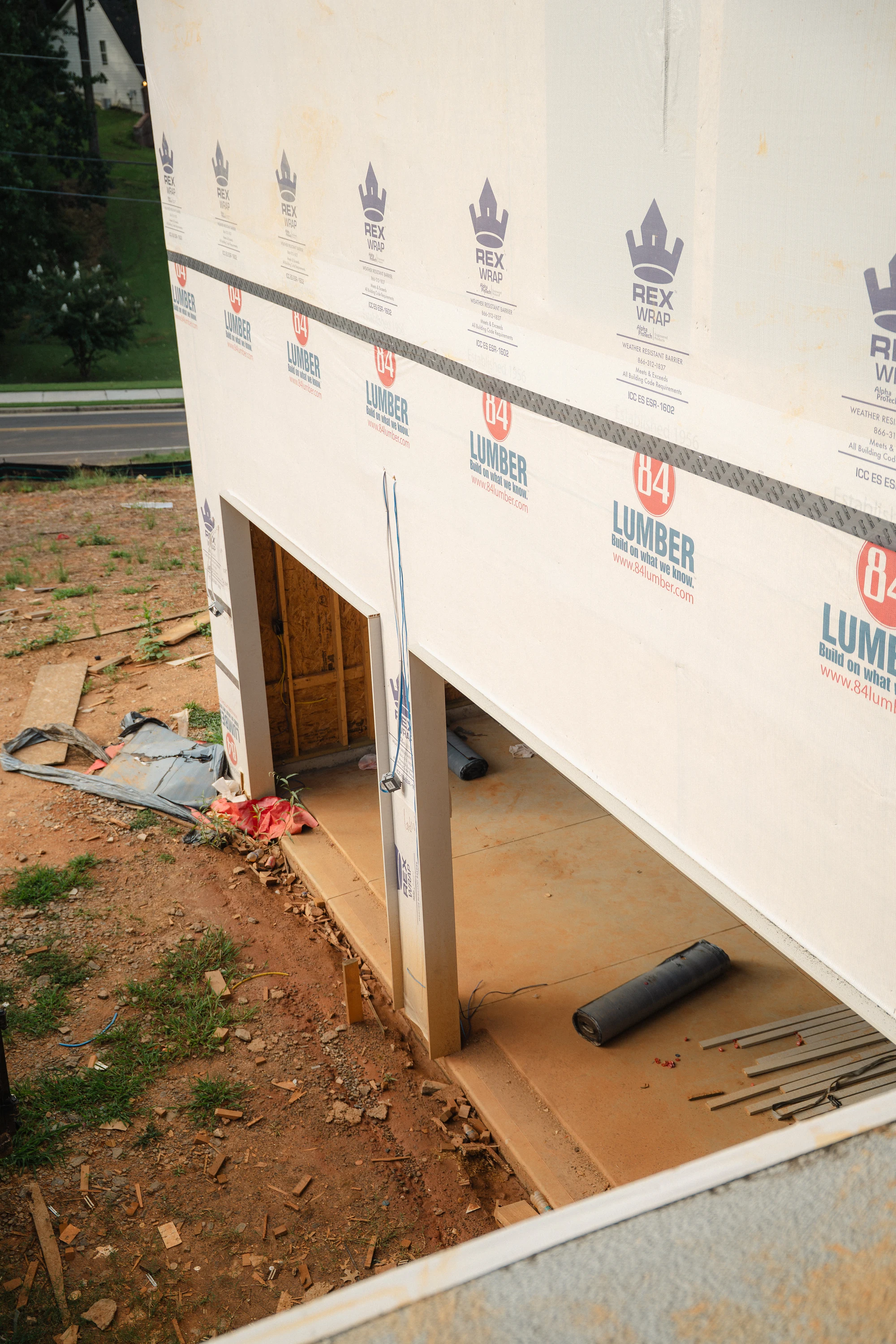 High-angle view of a wrapped exterior wall above two open lower-level bays and a concrete slab.