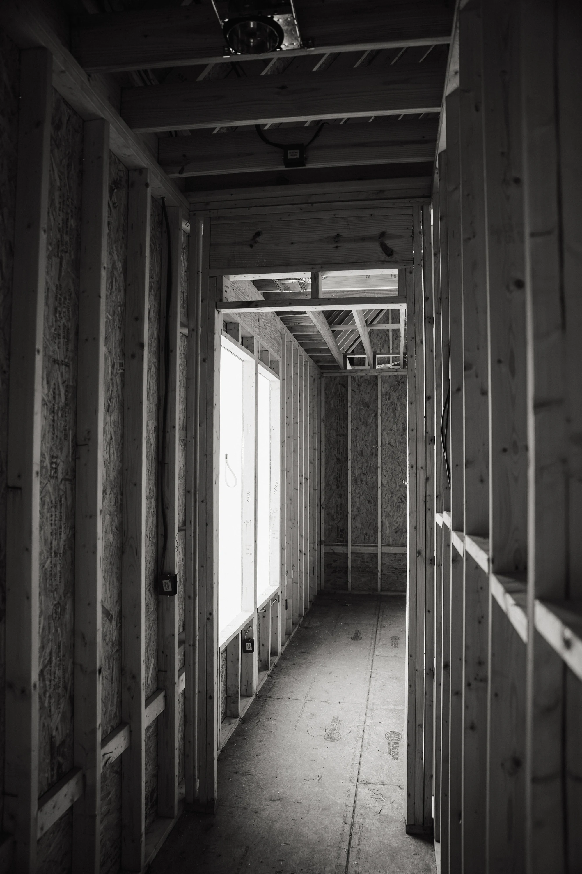 Black-and-white view down a framed corridor with open studs and ceiling joists.