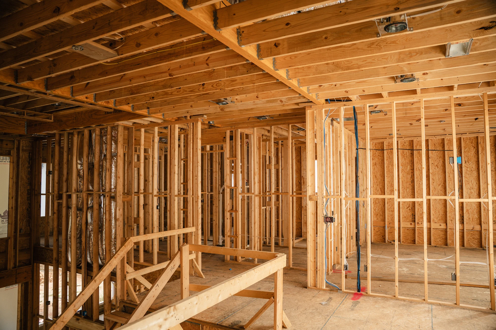 Open framed interior with ceiling joists, wall studs, utility lines, and temporary guardrails.
