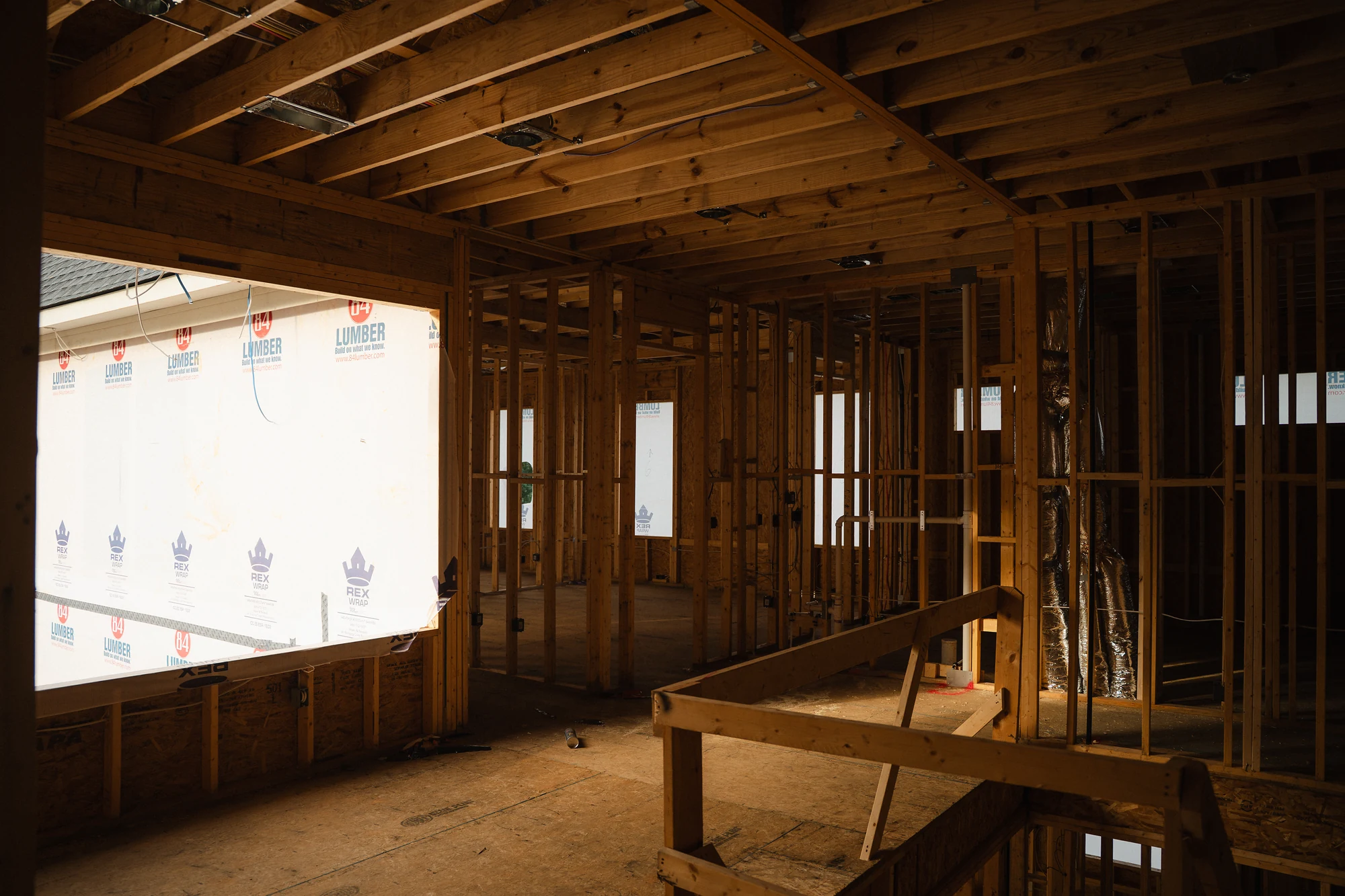 Framed upper-level space with a large exterior opening and temporary rails around a floor opening.
