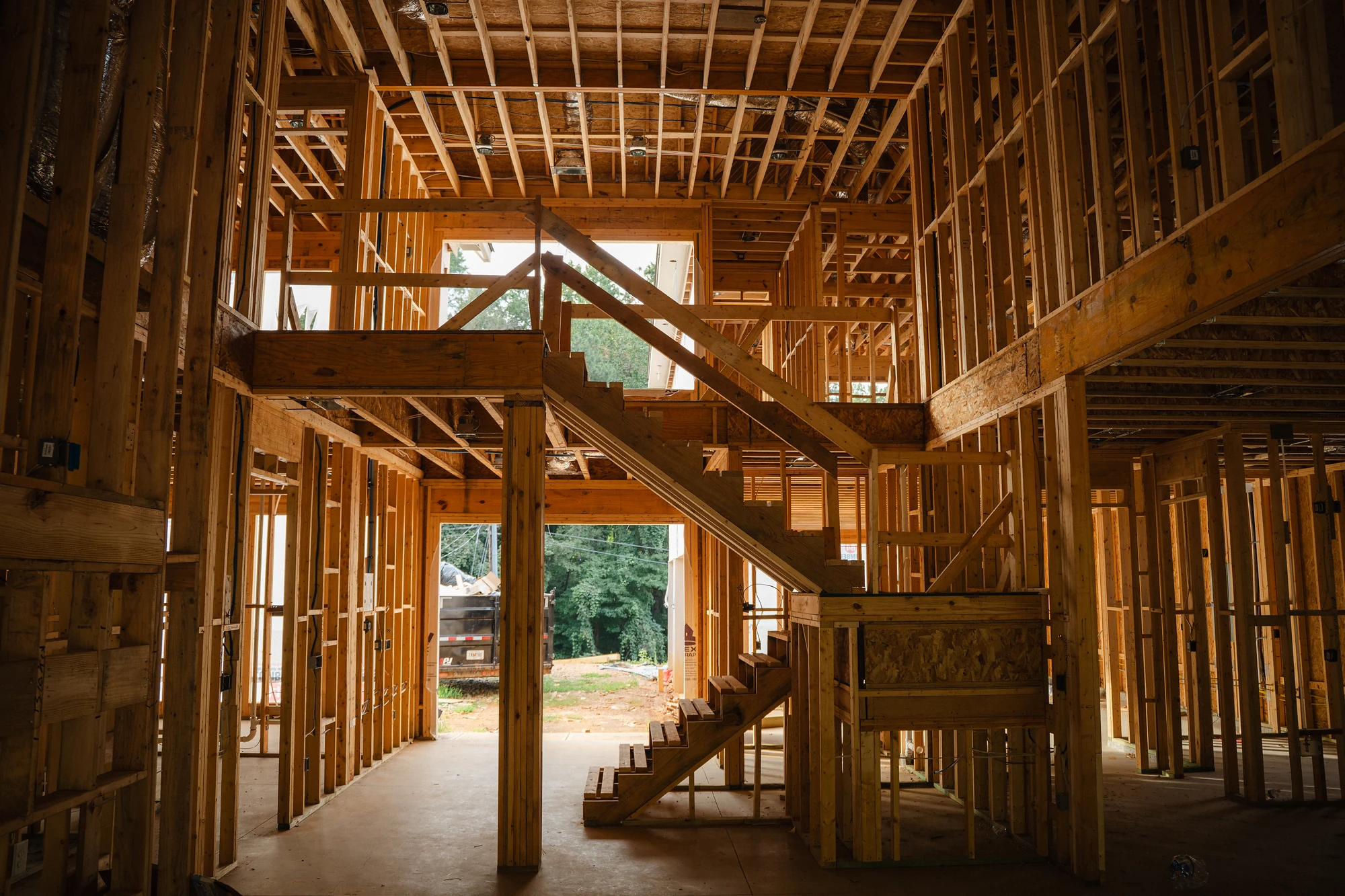 Two-story framed interior with wood stairs, open landings, wall studs, and ceiling joists.