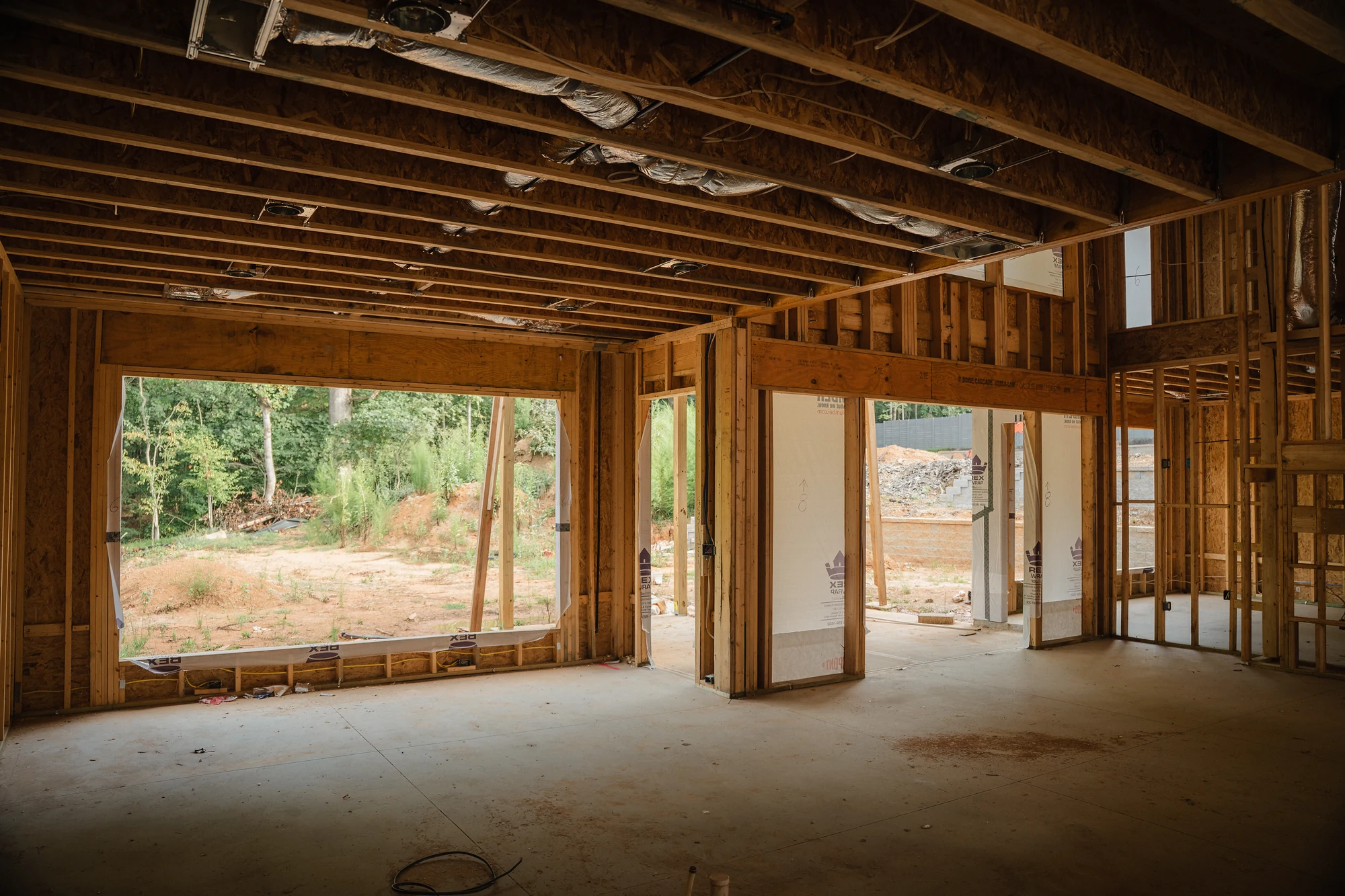 Large framed interior with exposed joists, wall studs, a concrete floor, and wide exterior openings.