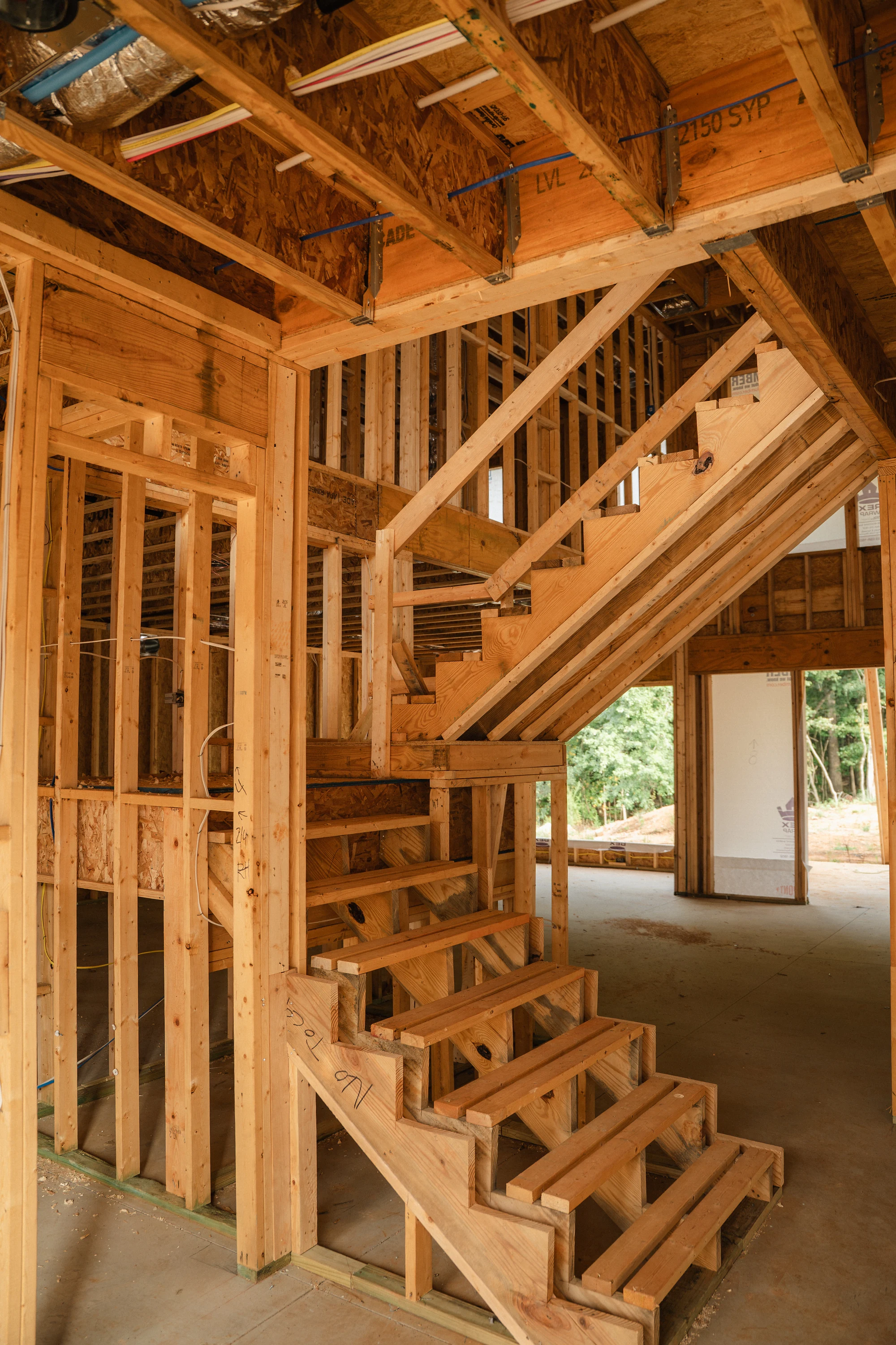 Close view of unfinished wood stairs and surrounding stud walls above a concrete floor.