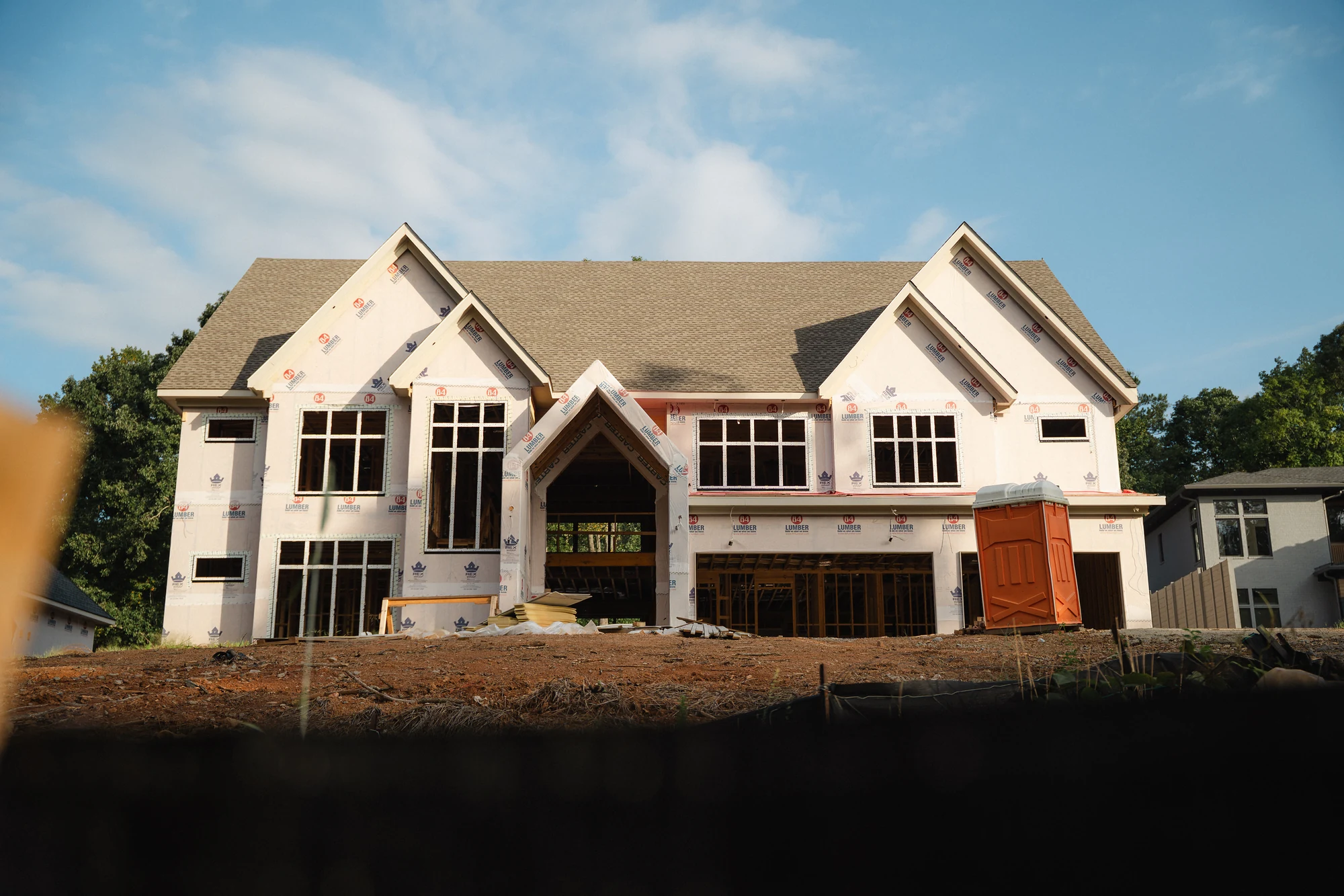 Wide front exterior of a roofed house with installed windows, wrapped walls, and open lower bays.