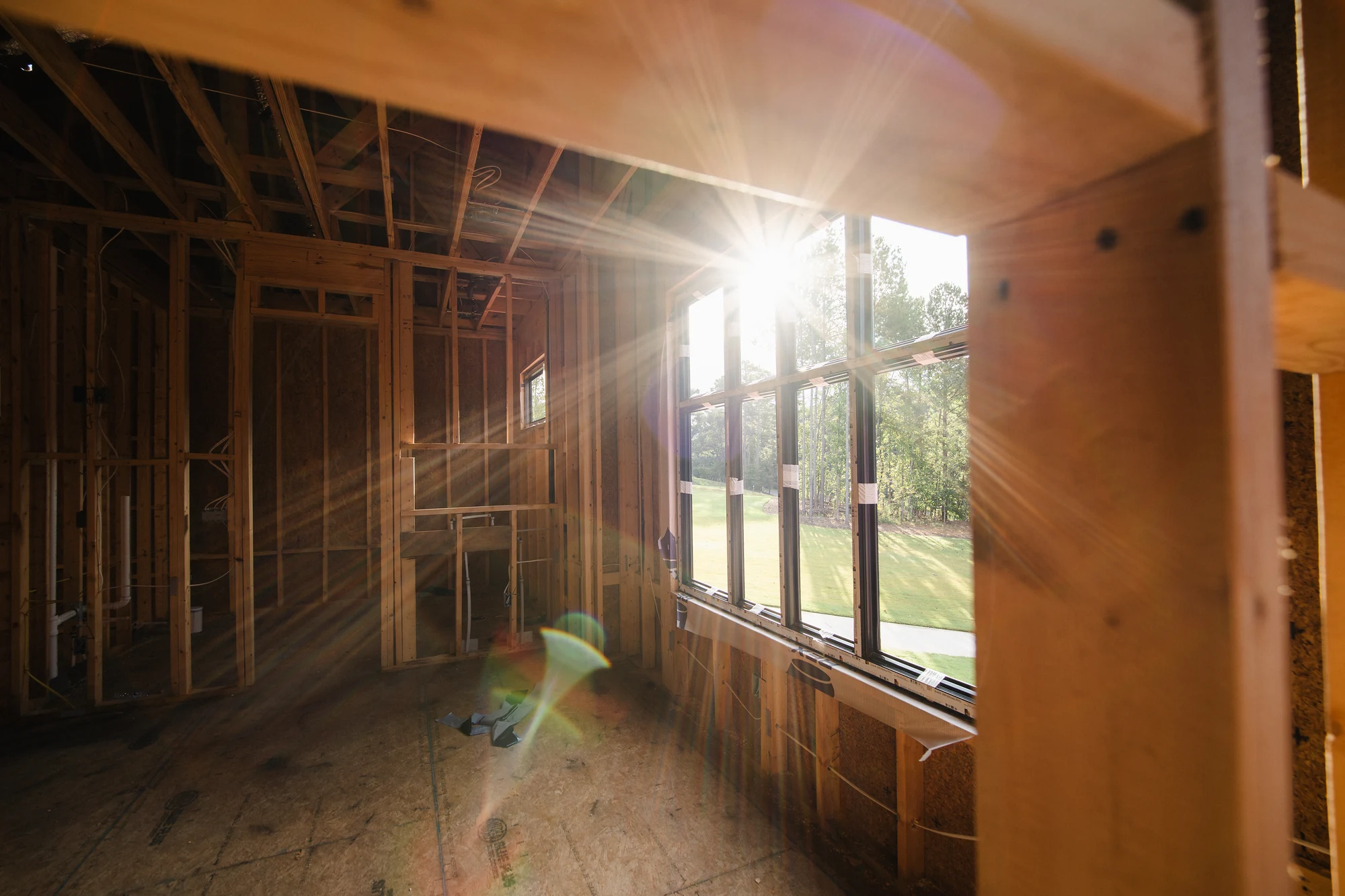 Sunlit framed interior with exposed studs, ceiling joists, and a row of installed windows.