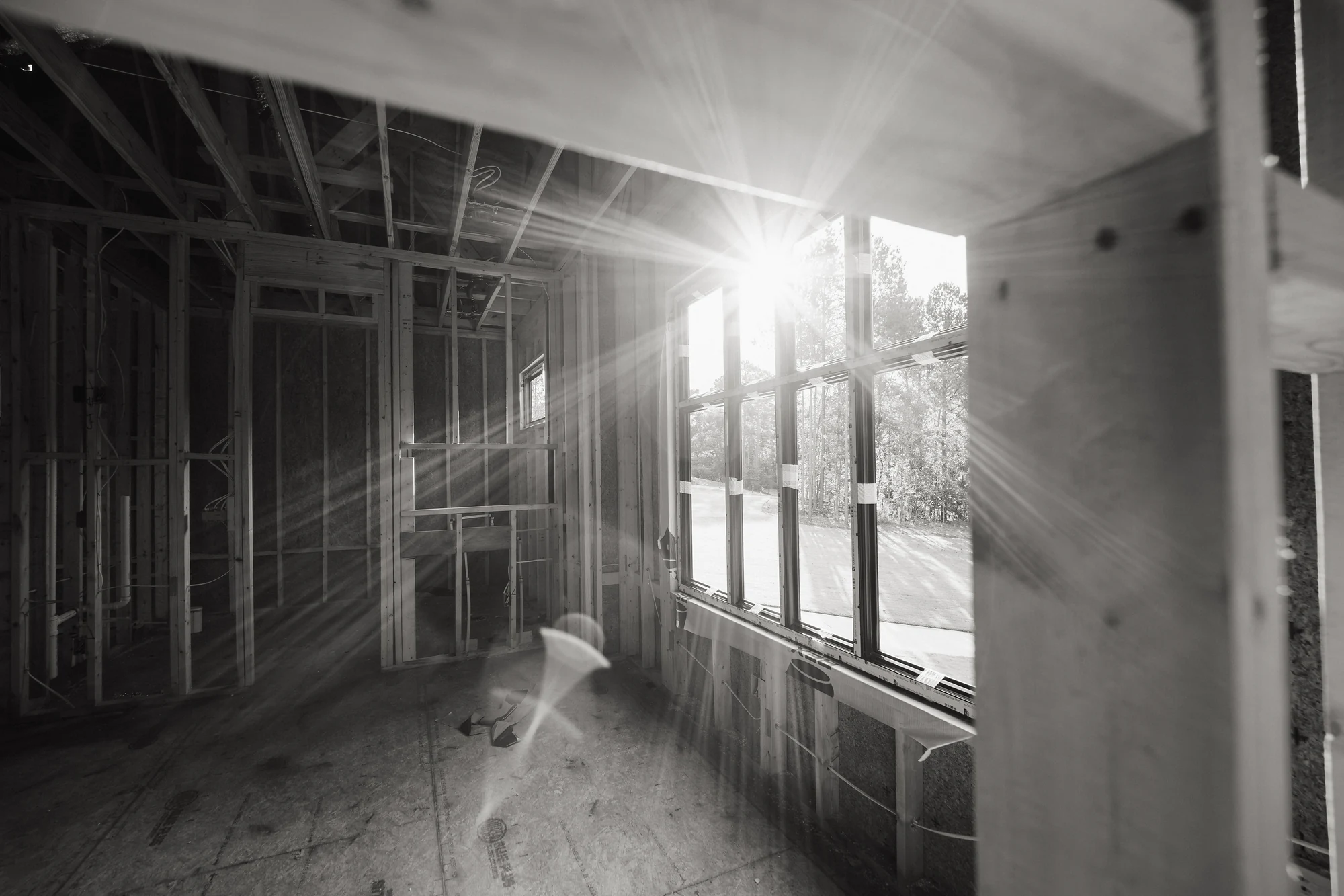 Black-and-white interior view with exposed framing and bright light through a window bank.