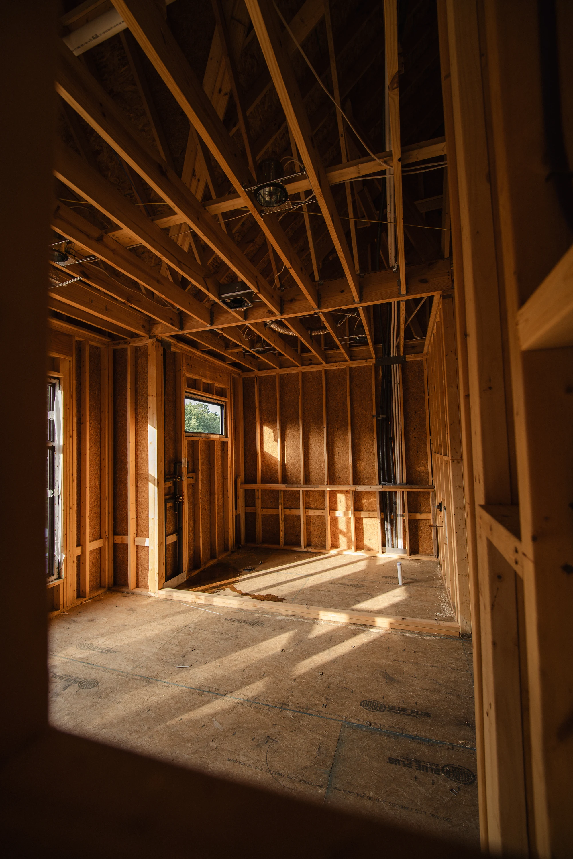 Narrow framed interior space with exposed ceiling joists, wall studs, and an installed window.