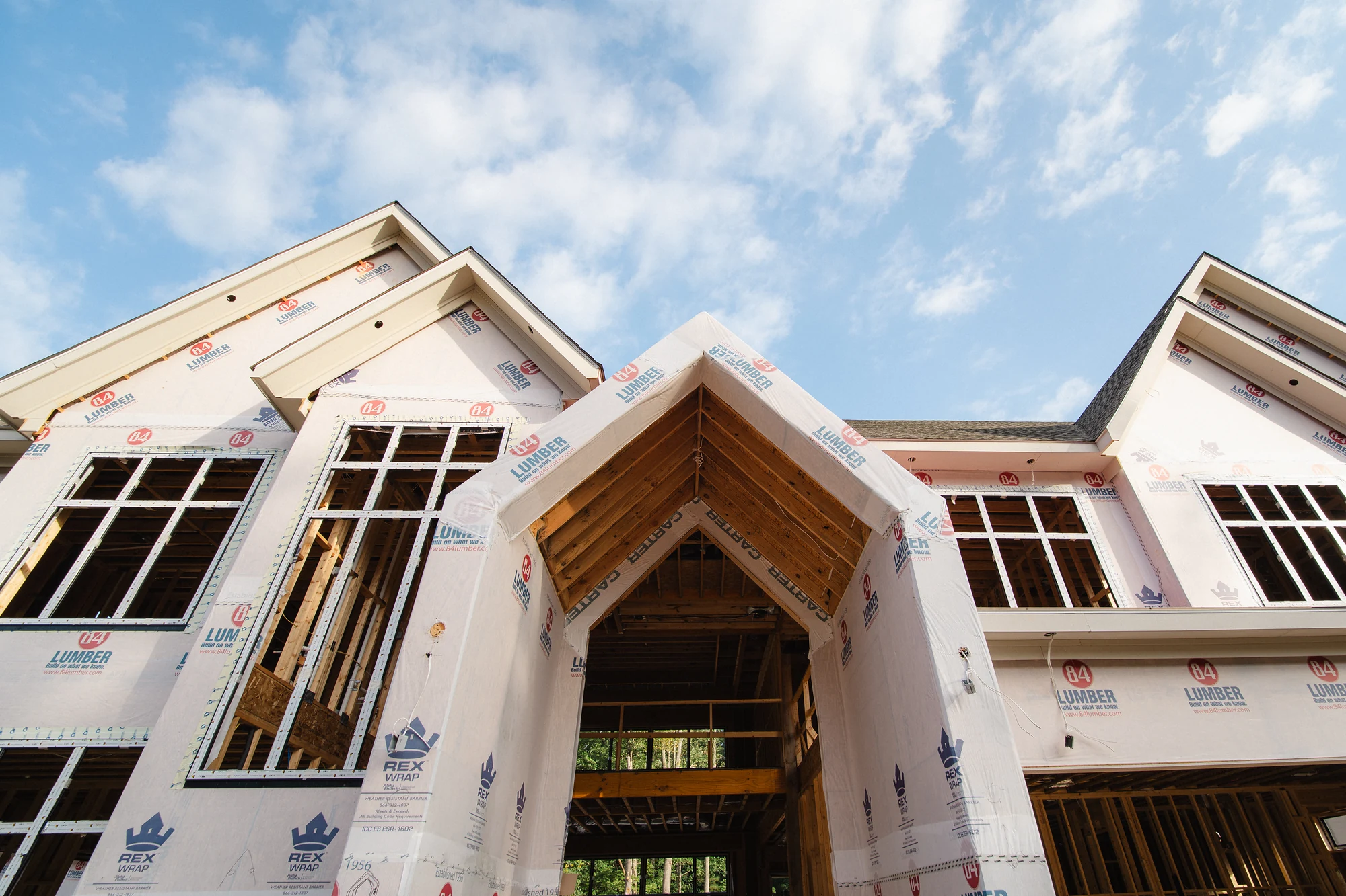 Upward view of a projecting gabled canopy with exposed wood framing and wrapped walls behind it.
