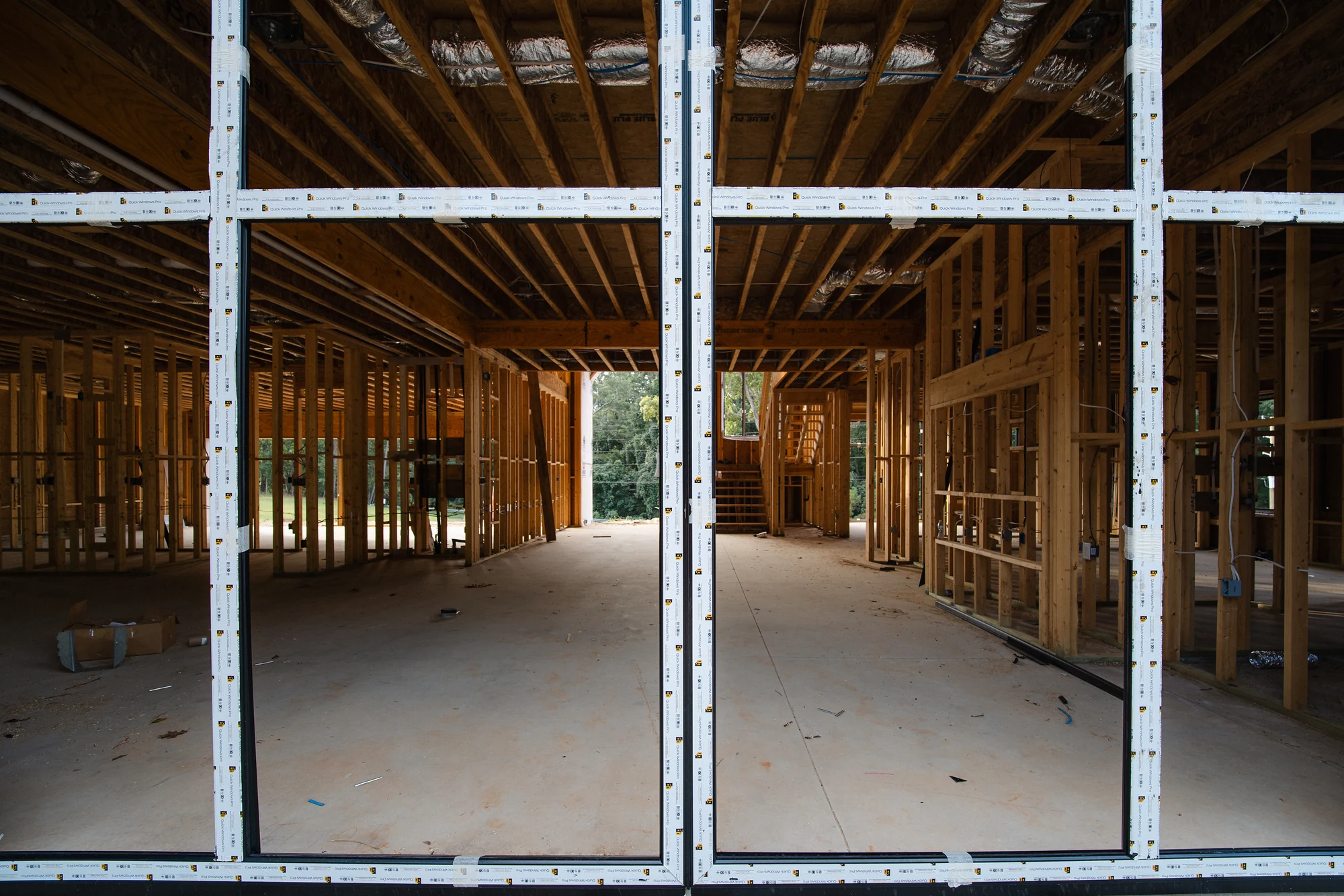 View through a large framed glazed opening into an open interior with exposed joists and studs.