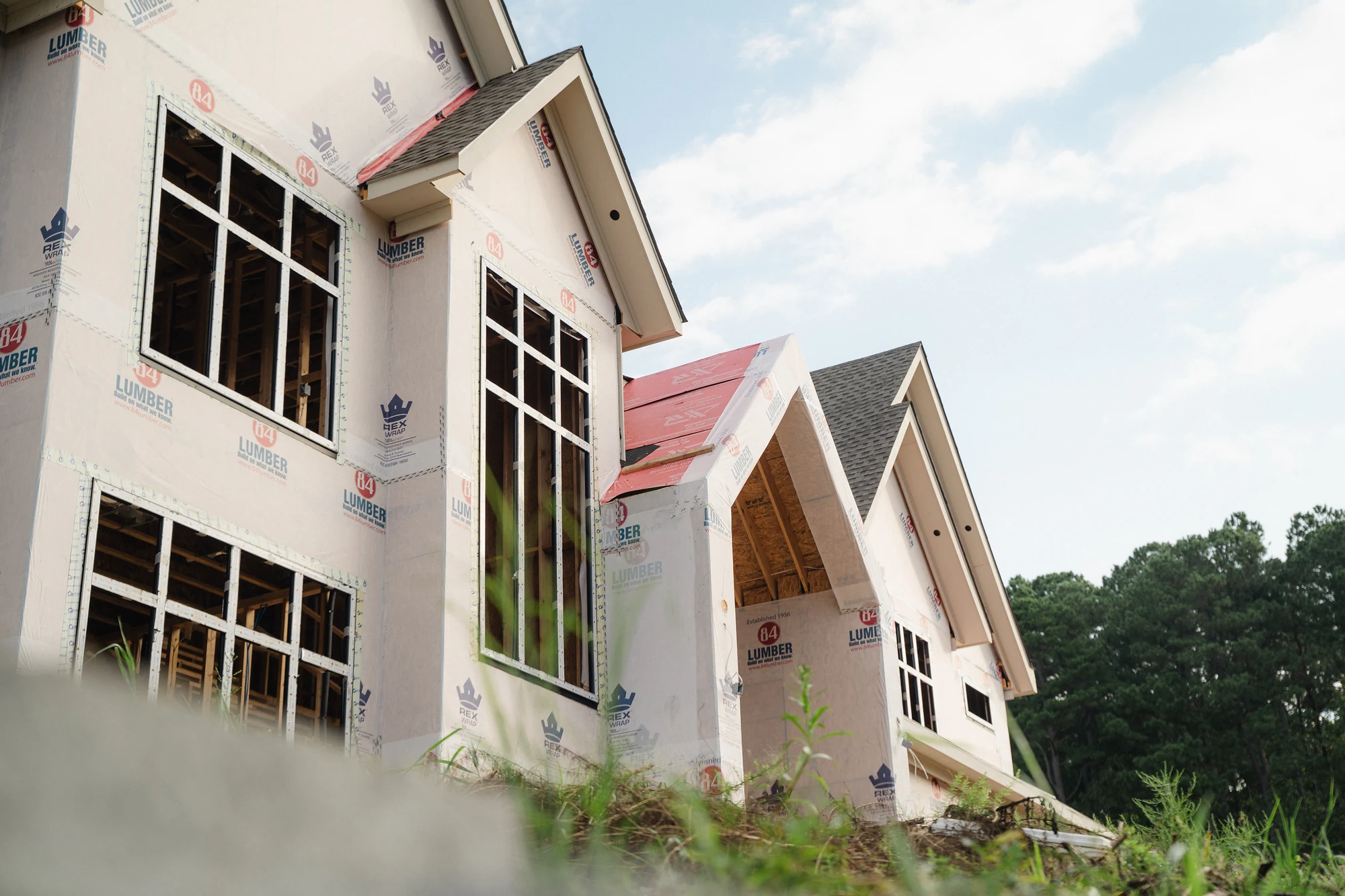 Side exterior with steep gables, installed windows, weather wrap, and exposed lower framing.