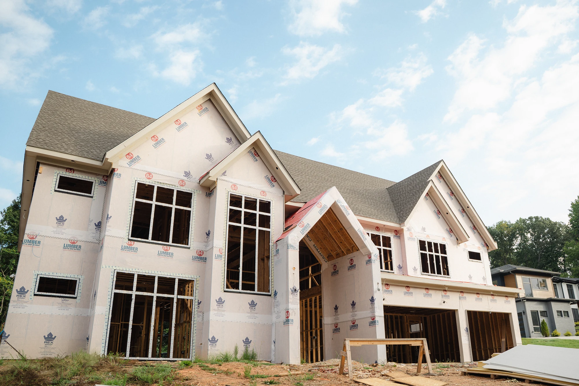Exterior corner with large installed windows, wrapped walls, and exposed framing at lower openings.