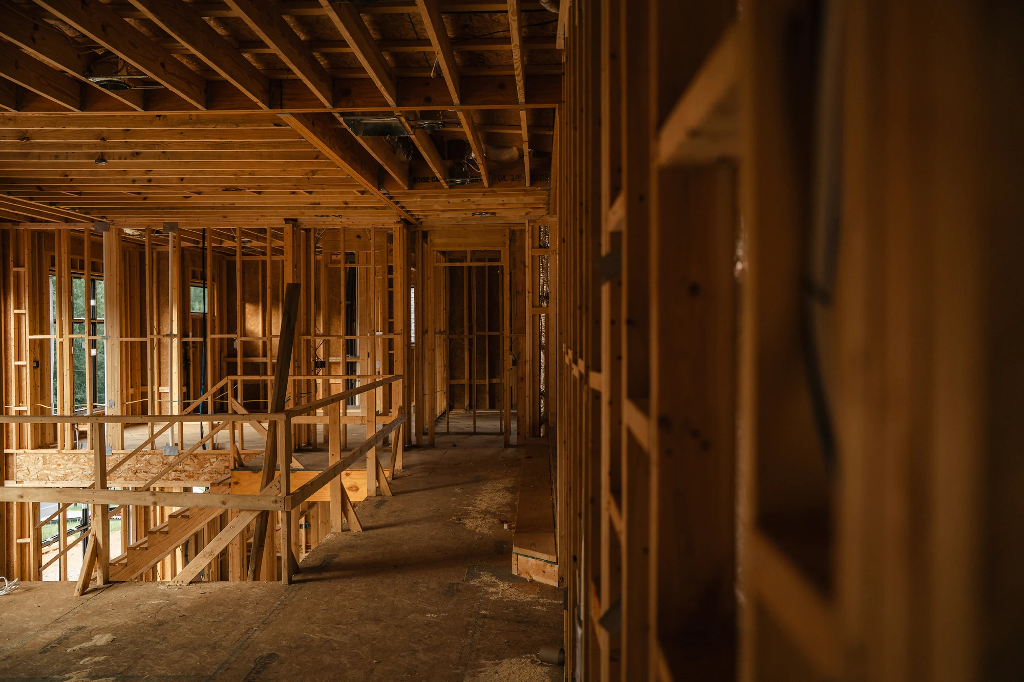Upper-level framed interior overlooking a stair opening with exposed joists and stud walls.