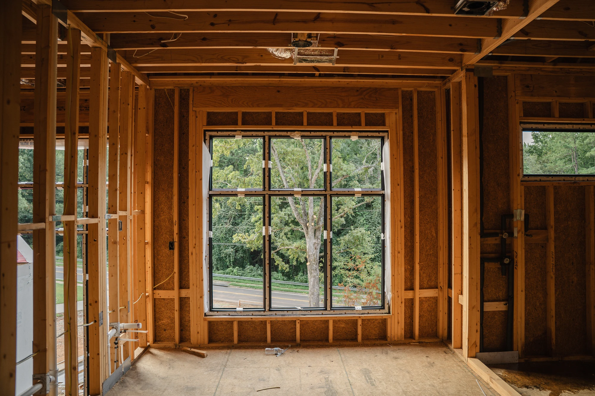 Framed interior area centered on a large installed window with exposed ceiling joists.