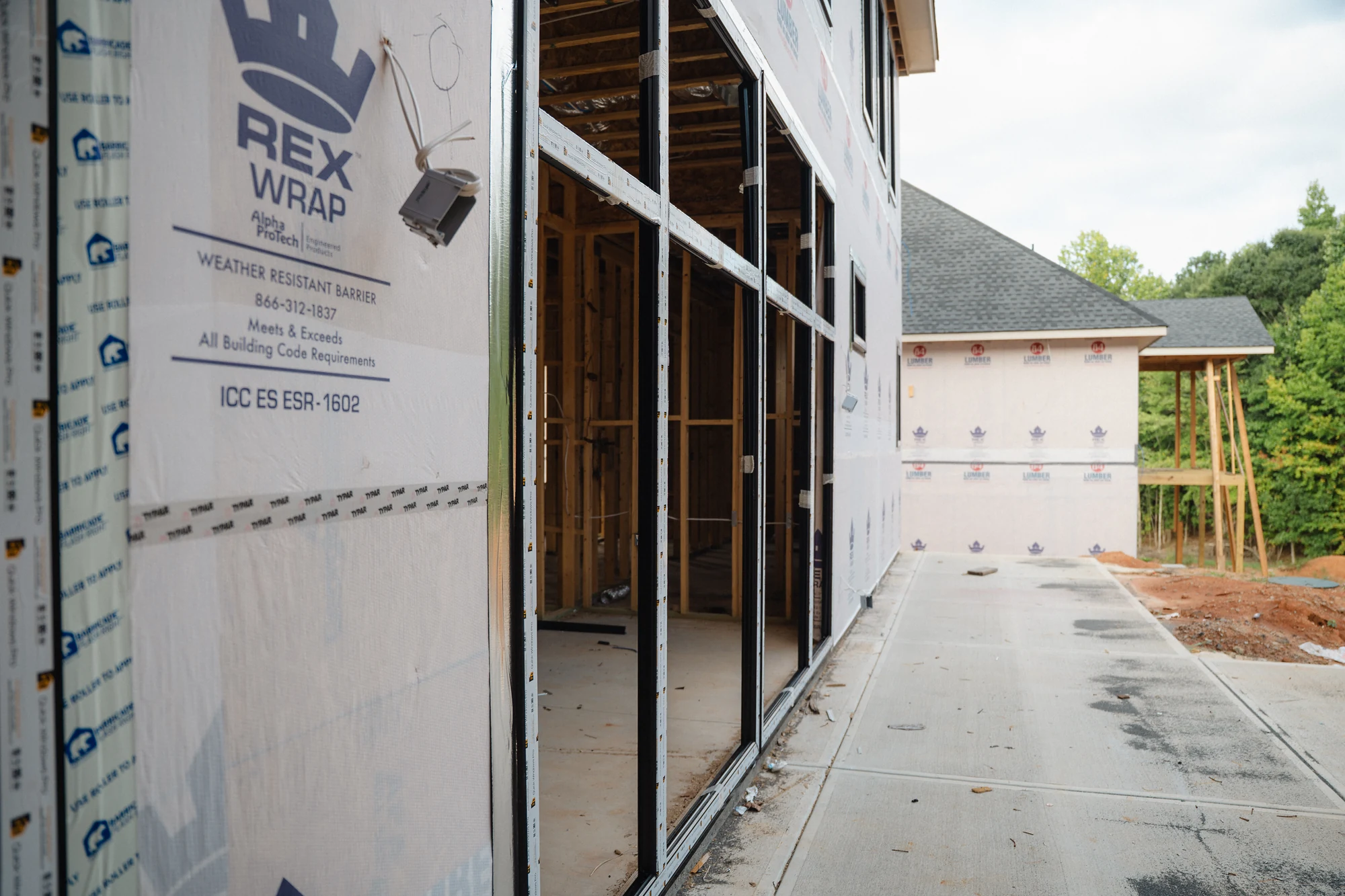 Concrete side passage beside wrapped walls, installed windows, and open framed doorways.