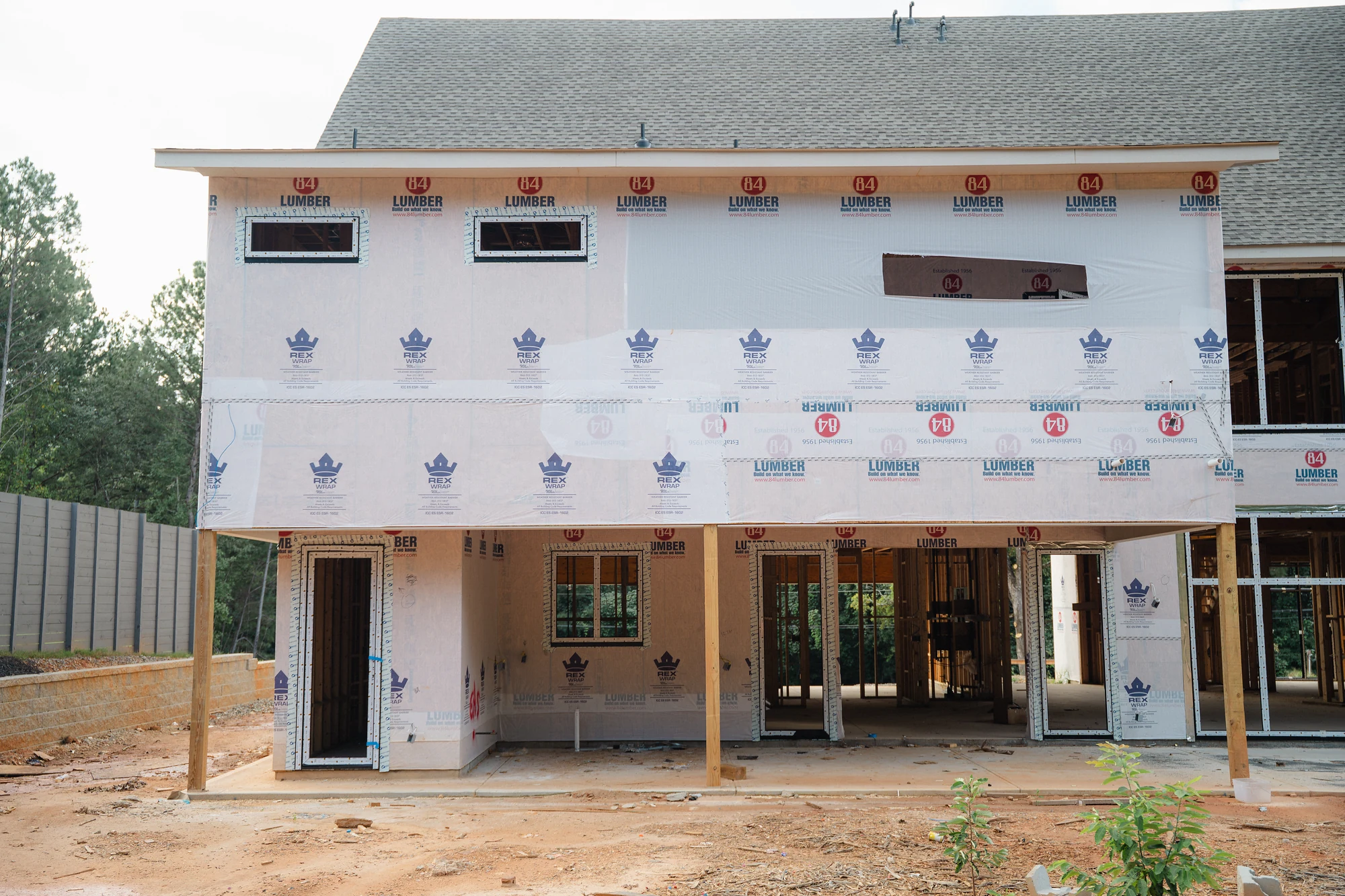 Straight-on exterior view of a wrapped two-story wall with window openings and three open lower bays.
